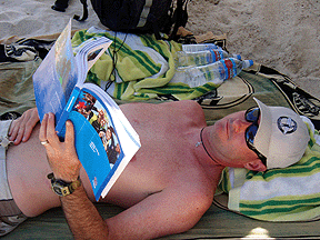 Jon reads the PADI textbook under a beach umbrella at the beach.
